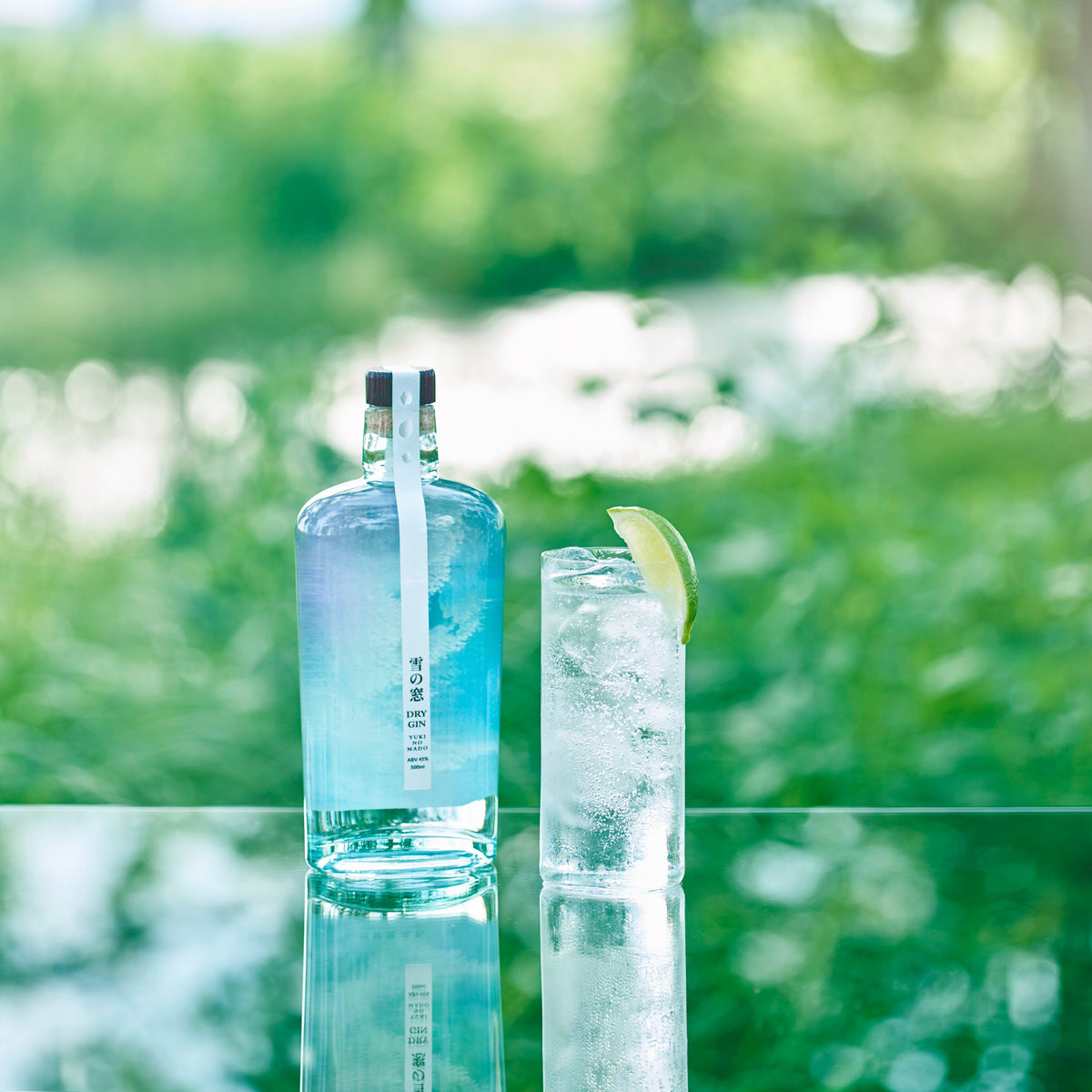 Yuki no Mado Dry Gin bottle with gin and tonic cocktail garnished with lime in an outdoor garden setting